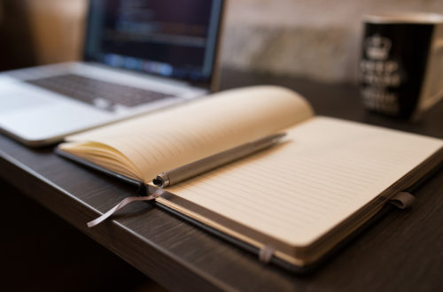 Picture of a computer, notebook, pen, and coffee mug sitting on a desk